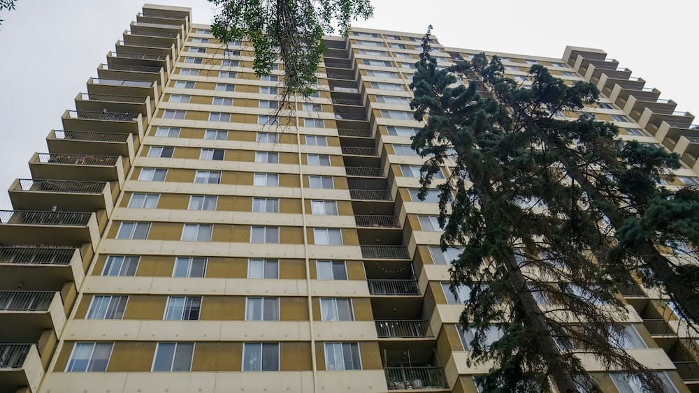 Edificio residencial alto cerca de 104 Street y 99 Avenue, en el centro de Edmonton, Alberta, Canadá, donde Samuel Jeffery vivía antes, visto desde abajo entre árboles maduros.