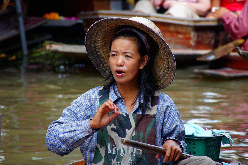 A candid photo of a Thai lady wearing a conical hat and army fatigue inspired apron at the Damnoen Saduak Floating Market in Bangkok, Thailand 