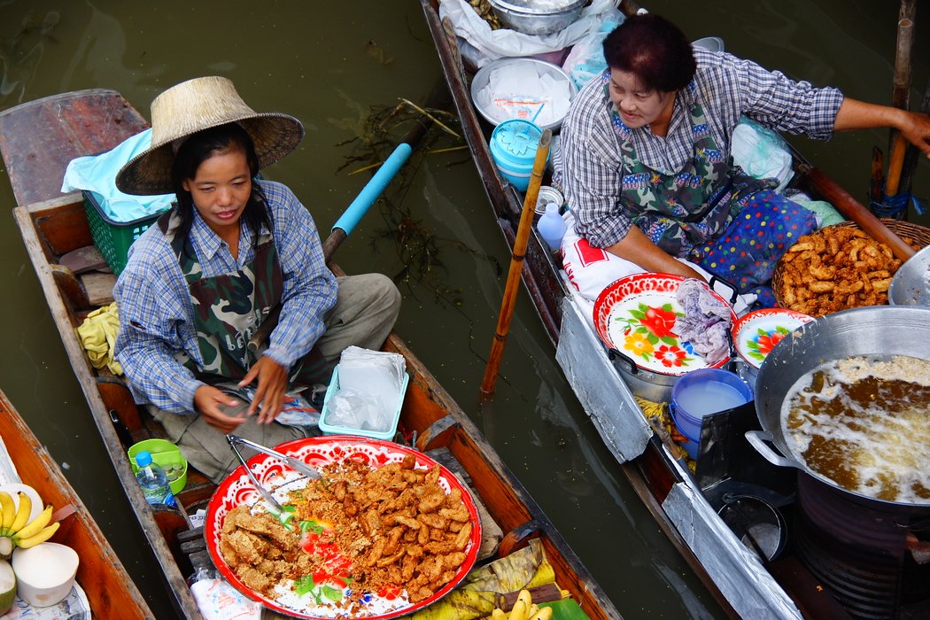 A friendly exchange between two Thai vendors both selling deep fried banana wedges at the Damnoen Saduak Floating Market in Thailand 