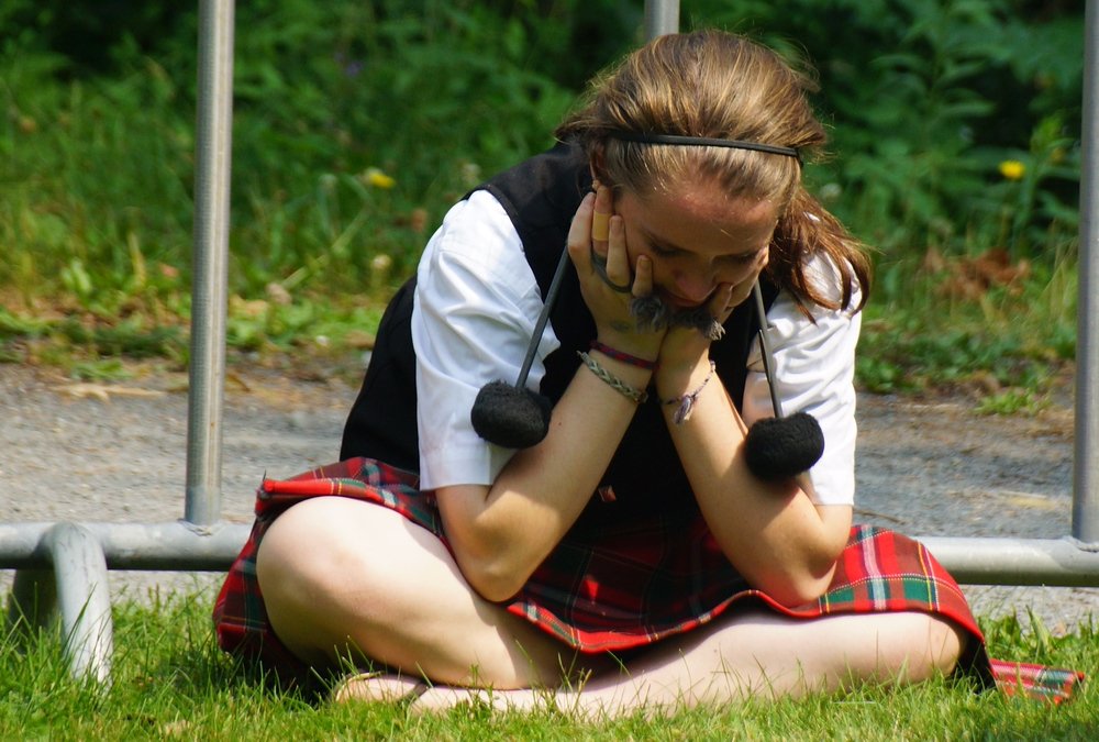 A girl sits down to take a break while resting her hands on her face at the New Brunswick Highland Games