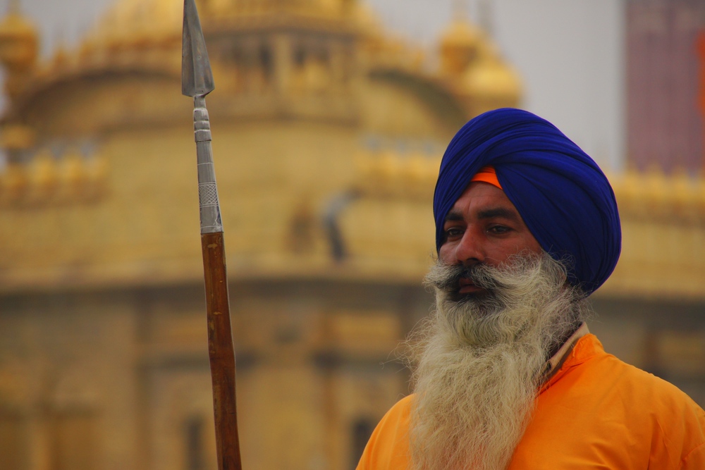 A guard with a most impressive beard stands tall outside of the main entrance to the Harmandir Sahib.