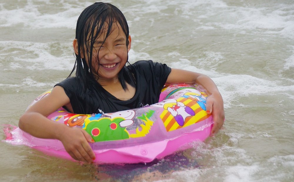 A Korean girl flashes an authentic smile while enjoying a moment splashing around in a floating tube at Daecheon Beach, Korea