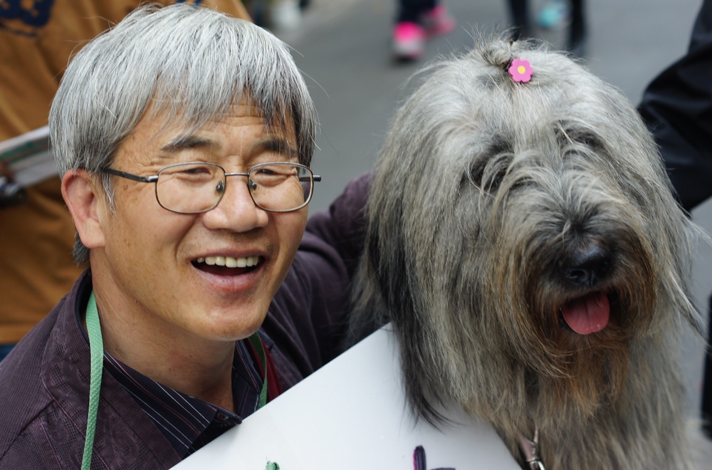 A Korean man wearing glasses and a big grin hugs his dog in Insadong, Seoul, South Korea.