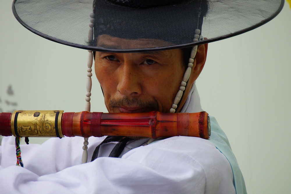 A Korean man wearing traditional attire plays a traditional instrument delighting passing pedestrians in Insadong, Seoul, South Korea