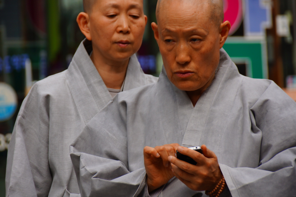 A Korean monk wearing a grey robe texts into messages using his cellphone. I'm at surprised at how many monks I can see in Insadong.