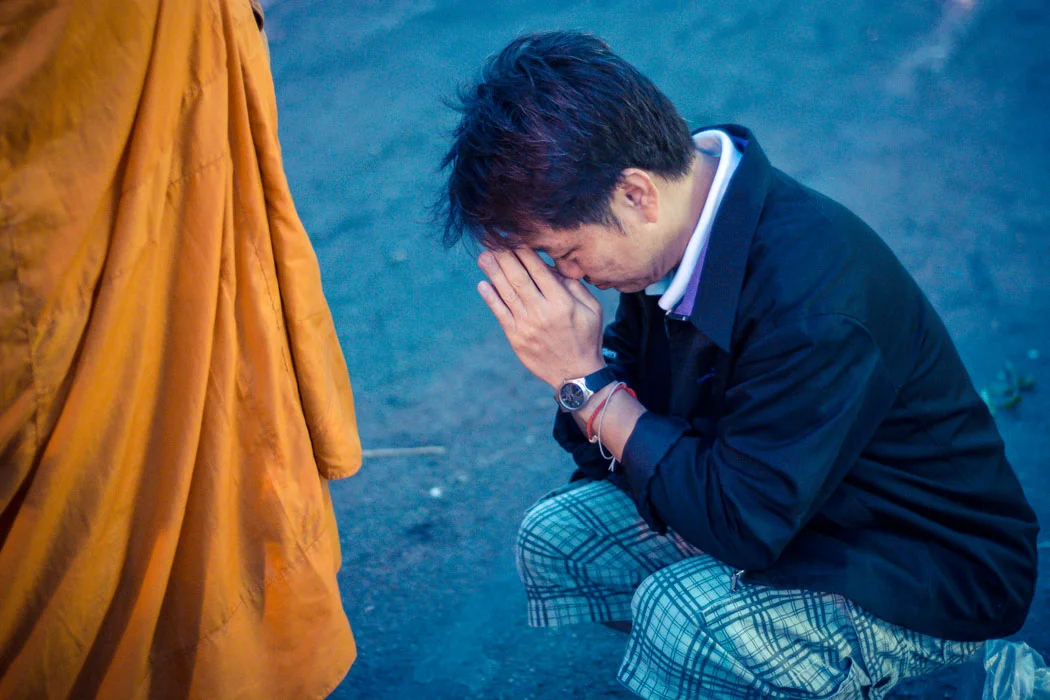 A local deeply concentrated in his early morning prayer to a Buddhist monk during the alms giving ritual, on the streets of Chiang Mai, Thailand. 
