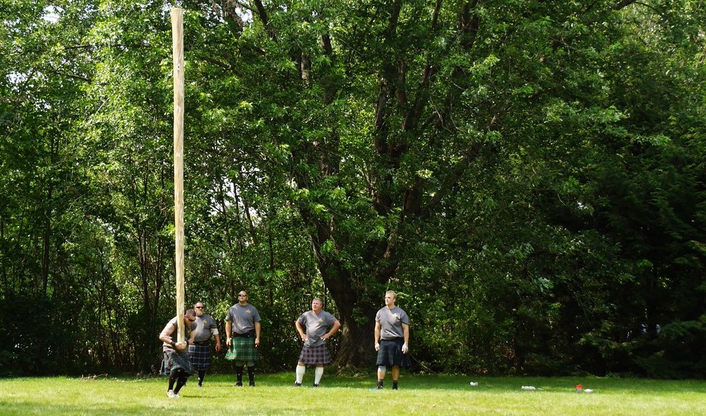 A man lifting a caber vertically before throwing it at the Highland Games in New Brunswick