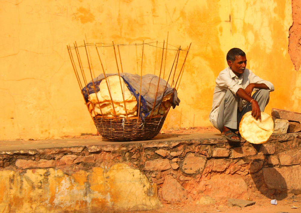 A man sits outside on the ledge with has basket of crispy flat-bread in Jaipur, India