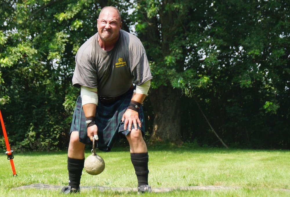 A man with a distinct facial expression of physical strain as he tries to toss a heavy weight over his head