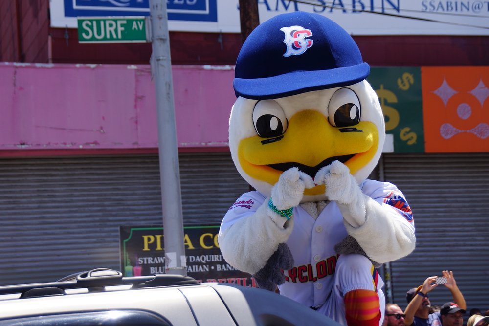 A New York City baseball mascot pointing at the crowd as it parades down the Coney Island Mermaid Parade