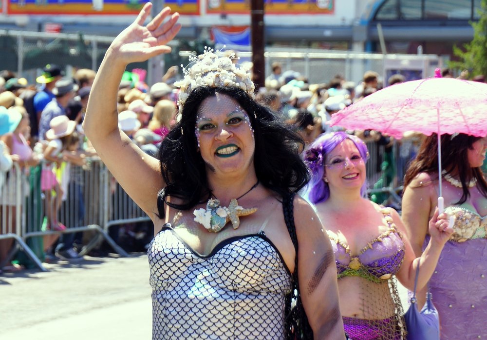 A performer in a Mermaid costume waving as she walks down the street in New York City