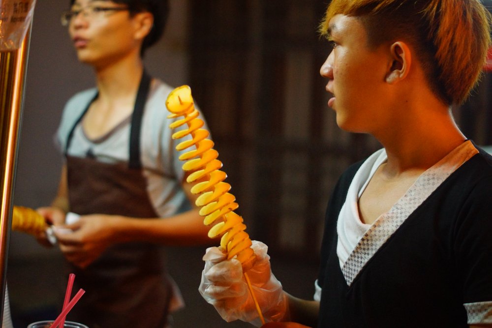 A street vendor prepares strips of potatoes on skewer that are known as tornado chips. I've had something very to this in South Korea in Malacca, Malaysia