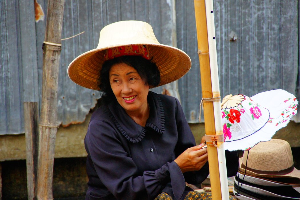 A Thai lady vendor with a collection of hats for sale flashes a smile at the Damnoen Saduak Floating Market in Bangkok, Thailand