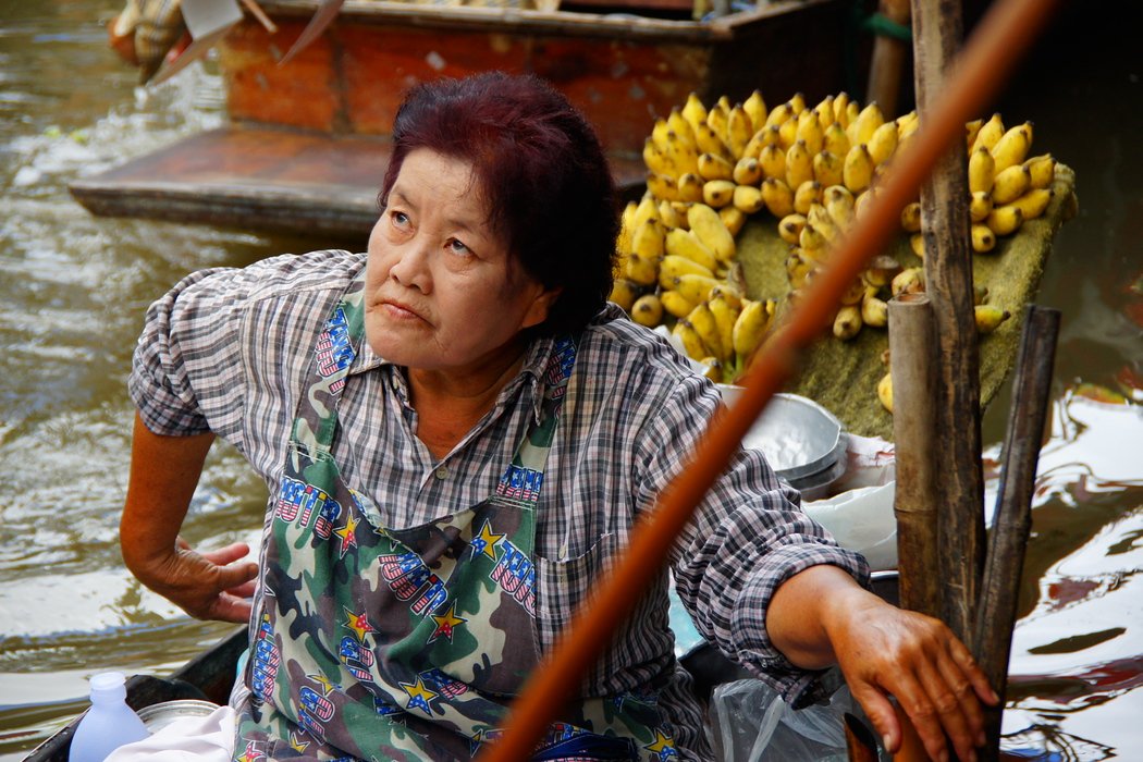 A Thai lady with dyed hair makes eye contact with a group of tourists at the Damnoen Saduak Floating Market in Thailand 