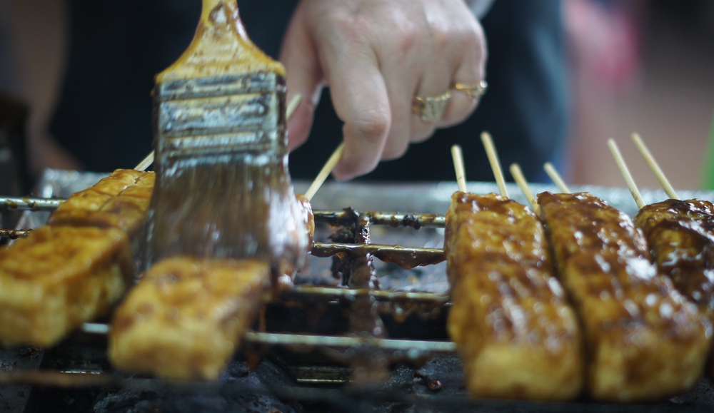 A vendor brushes the stinky tofu (臭豆腐) that lays skewered on the grill at a night market in Taipei