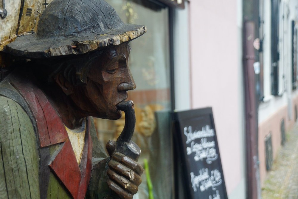 A wooden sculpture of a man smoking a pipe just outside of a restaurant  bar in Freiburg, Germany