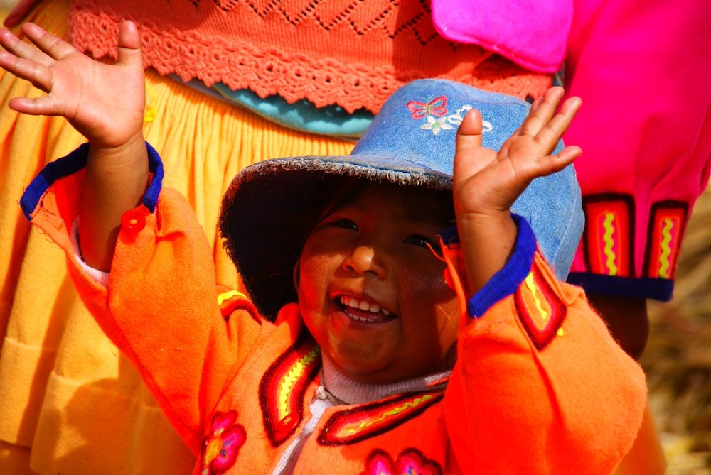 A young child dressed in traditional colourful clothes gleefully sings and performs for a group of tourists - Lake Titicaca, Peru. 