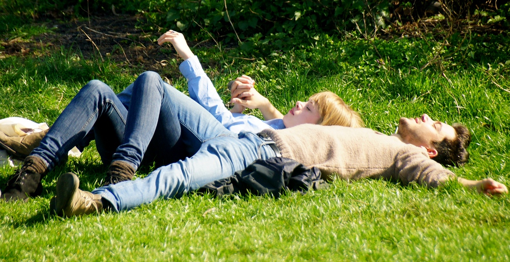 A young couple lying down on the grass soaking up the sun and atmosphere from the live musical performances. 