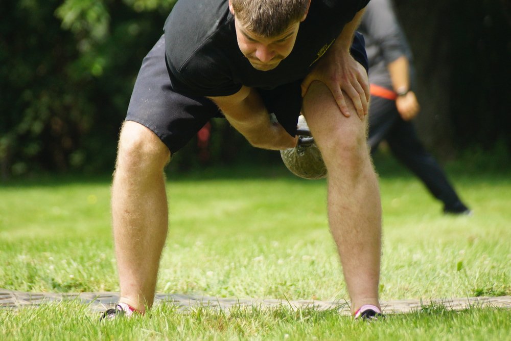 A young man crouches down swinging a weight below his legs prior to releasing it in the air at the Highland Games in Fredericton