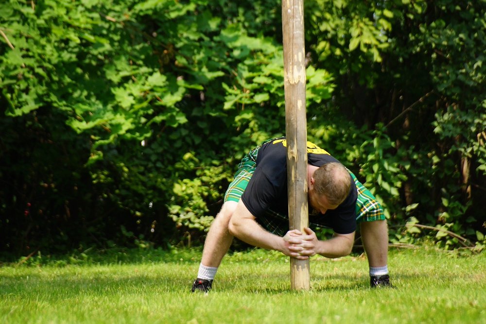 A young man is crouching down to life the caber to an upright position before tossing it at the Highland Games