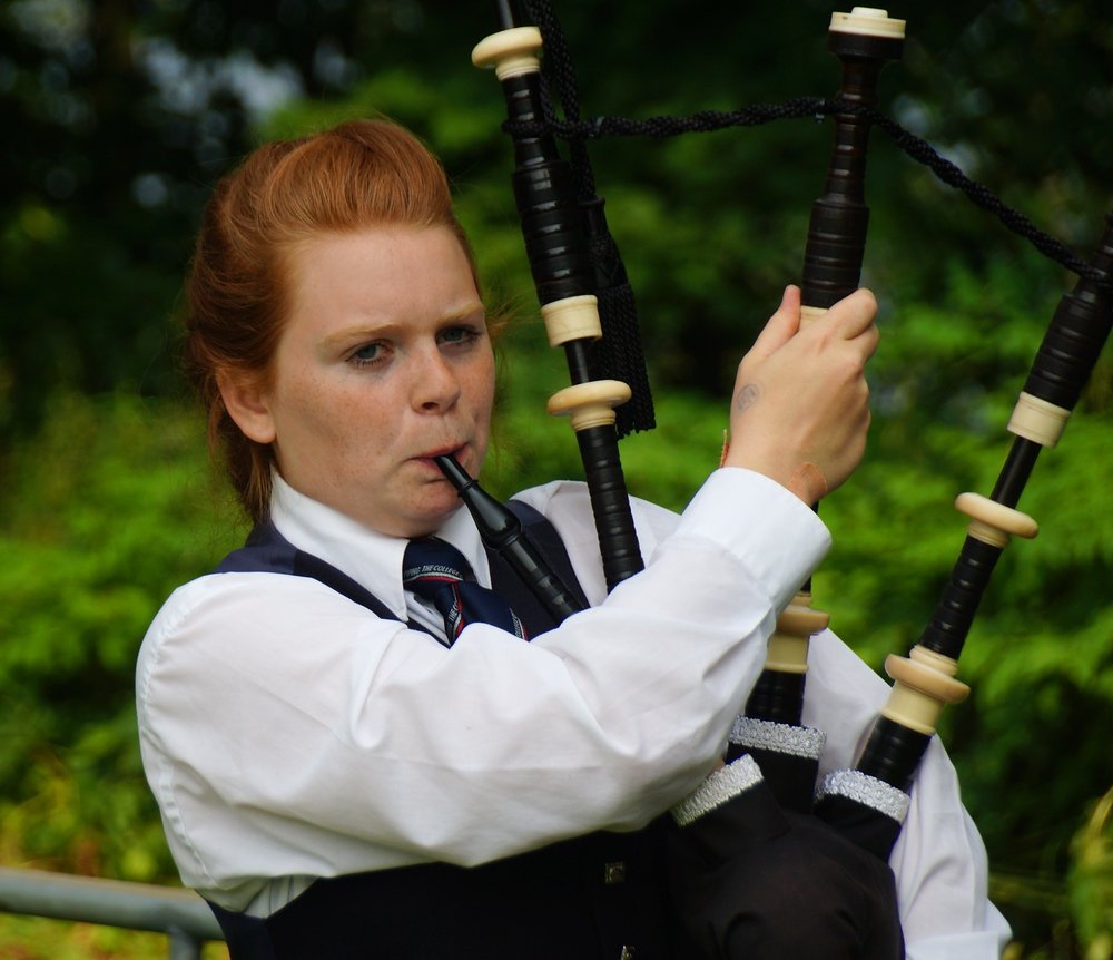 A young red headed lady warming up by playing the bagpipes before the competition started at the Highland Games