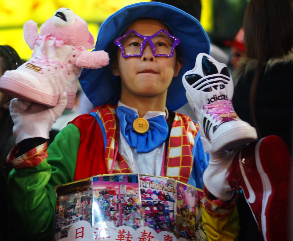 A young Taiwanese vendor dressed in funky attire tries to peddle shoes on the curb of the Shilin Market in Taipei, Taiwan