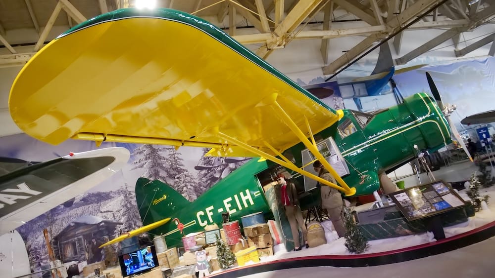 El avión de monte verde matriculado como CF-EIH, con alas amarillas, se exhibe en un diorama montado de una cabaña de invierno con carga y figuras de maniquíes en el Alberta Aviation Museum en Edmonton, Alberta, Canadá.