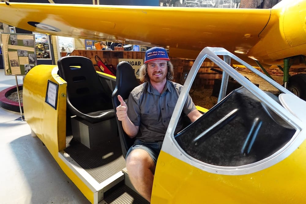 Samuel Jeffery en la cabina de un avión del Alberta Aviation Museum, Edmonton, Alberta, Canadá Samuel Jeffery está sentado dentro de la cabina amarilla de un avión en exhibición en el Alberta Aviation Museum, Edmonton, Alberta, Canadá, haciendo pulgar arriba bajo el ala de una aeronave antigua.