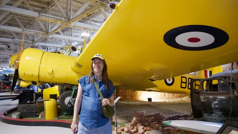 Audrey Bergner Beside a Yellow Aircraft at the Alberta Aviation Museum in Edmonton, Alberta, Canada Audrey Bergner standing beneath the wing of a bright yellow aircraft inside the Alberta Aviation Museum in Edmonton, Alberta, Canada, with aviation displays arranged throughout the historic hangar.