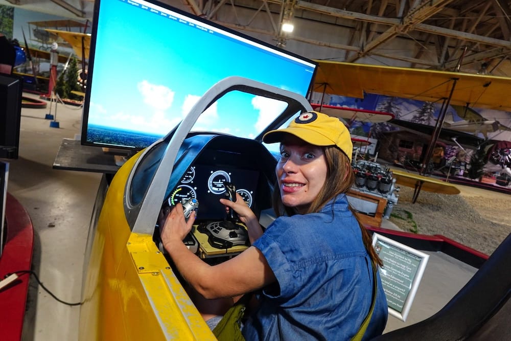 Audrey Bergner maneja la palanca y el panel de instrumentos dentro de la cabina del simulador de vuelo en el Alberta Aviation Museum en Edmonton, Alberta, Canadá, con una pantalla de vuelo visible adelante.