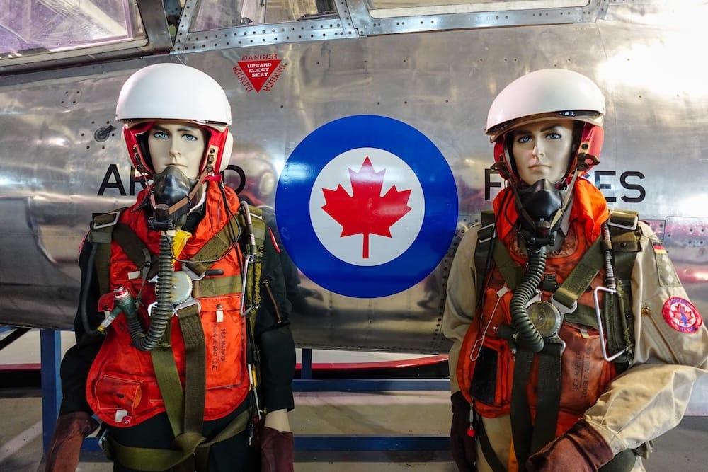 Dos maniquíes con equipo de vuelo clásico para pilotos de las Fuerzas Armadas Canadienses, incluyendo cascos y máscaras de oxígeno, parados frente al fuselaje de un jet con una escarapela de la Royal Canadian Air Force en el Alberta Aviation Museum en Edmonton, Alberta, Canadá.