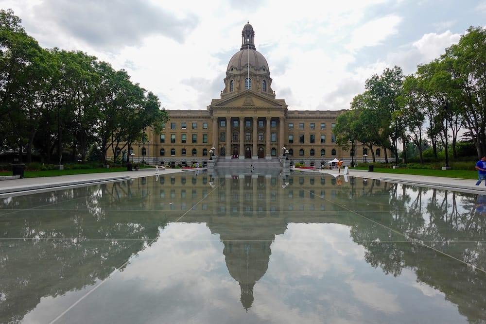 Edificio de la Legislatura de Alberta y estanque reflectante en Edmonton, Alberta, Canadá El edificio de la Legislatura de Alberta, en Edmonton, Alberta, Canadá, se alza detrás de un amplio estanque reflectante, con su fachada de piedra, cúpula central, árboles y cielo nublado reflejados en el agua.