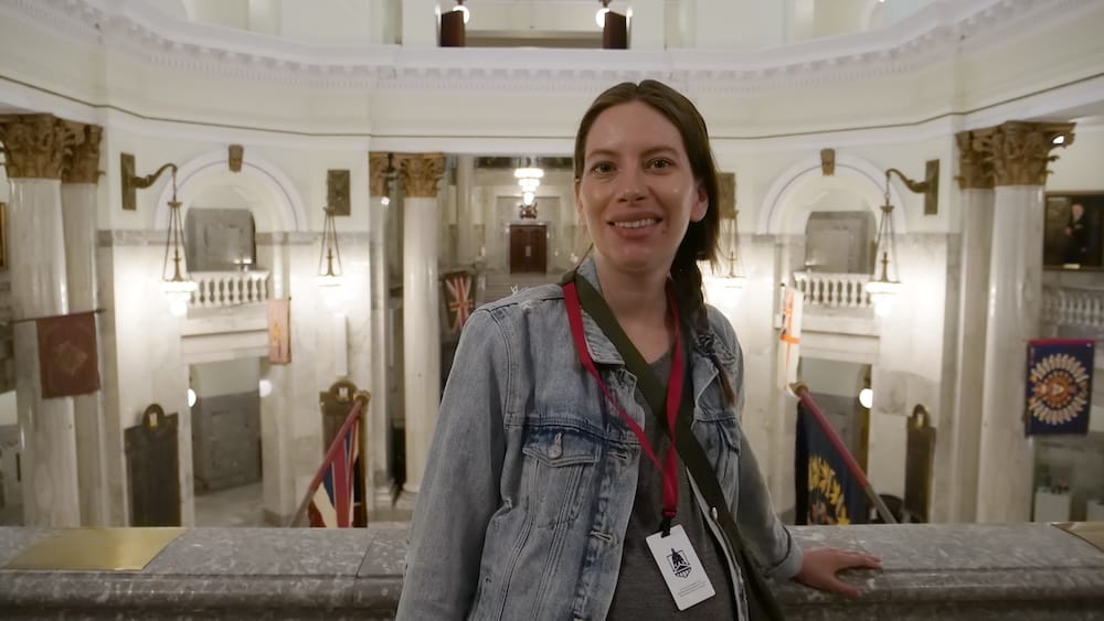 Audrey Bergner on a guided tour inside the Alberta Legislature rotunda in Edmonton, Alberta, Canada Audrey Bergner stands inside the Alberta Legislature during a guided tour in Edmonton, Alberta, Canada, with her visitor pass visible against the marble rotunda, columns, arches and historic flags behind her.
