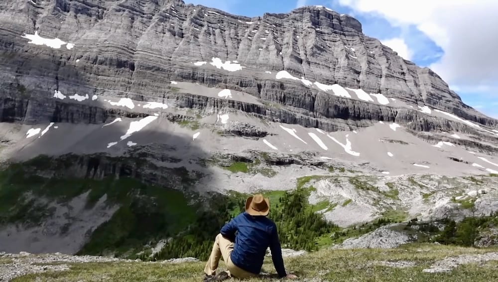 Samuel Jeffery taking in the mountain scenery at Allenby Pass in Banff National Park, Alberta, Canada Samuel Jeffery sits on a rocky alpine slope at Allenby Pass in Banff National Park, Alberta, Canada, looking toward a massive layered mountain wall streaked with lingering snow.