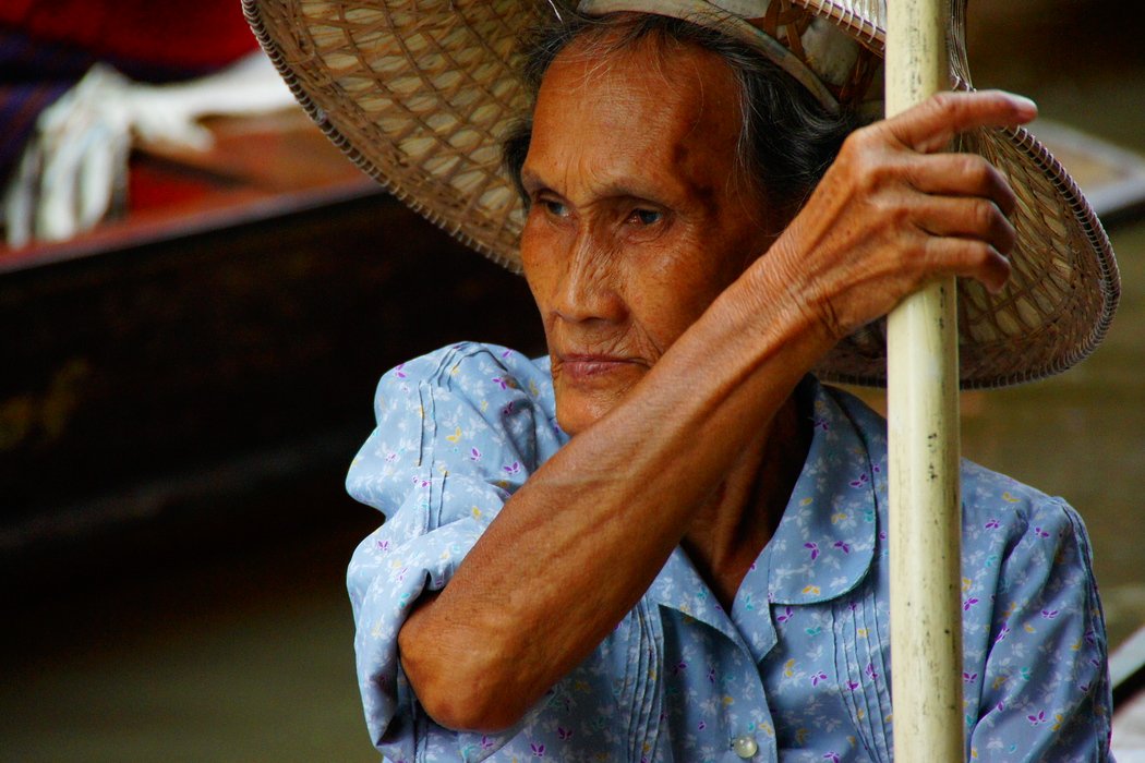 An elderly Thai lady paddles here way down the canal in a tiny vessel while trying to avoid colliding with much larger ones at the Damnoen Saduak Floating Market in Bangkok, Thailand