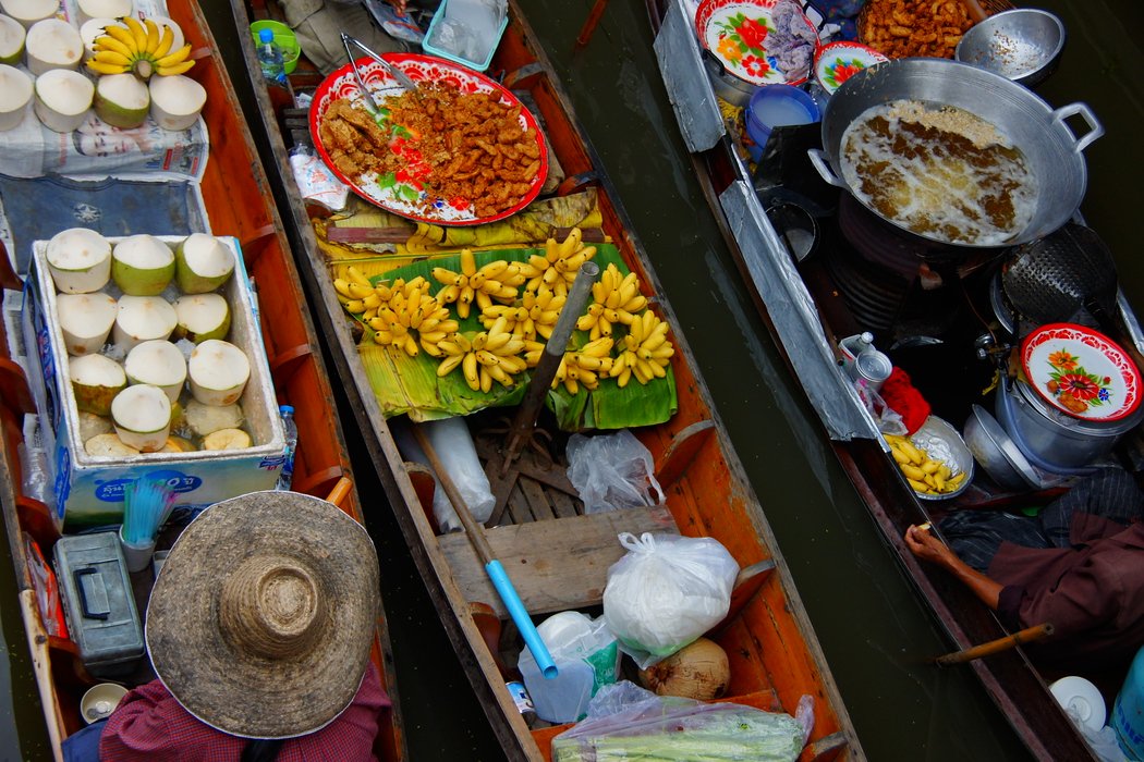 An overhead perspective travel photo of three rowboats filled with fruit (bananas and coconuts) passing each other at the same time at the Damnoen Saduak Floating Market in Thailand 