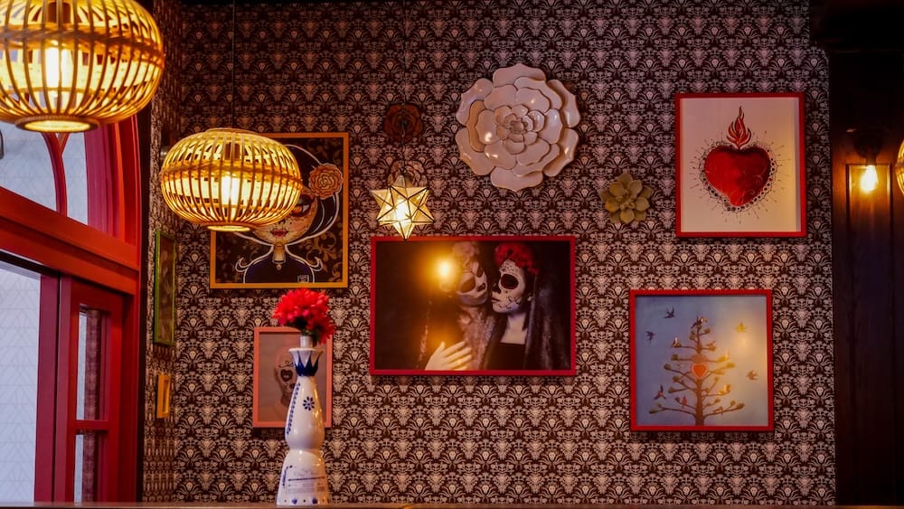 Añejo Restaurant interior decor and wall art in Banff, Alberta, Canada Interior of Añejo in Banff, Alberta, Canada, with patterned wallpaper, framed Mexican-inspired artwork, decorative flowers and warm woven pendant lights above the dining area.
