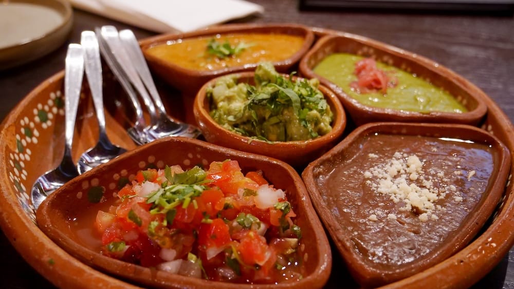 Degustación de salsas con guacamole y porotos refritos en Añejo, Banff, Alberta, Canadá Degustación de salsas y dips en Añejo, Banff, Alberta, Canadá, con pico de gallo, guacamole, porotos refritos y salsas verde y roja servidas en pequeños cuencos de barro sobre una fuente de cerámica.