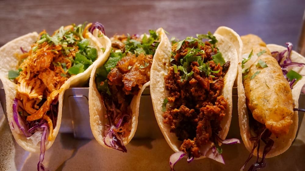Taco lineup at Añejo Banff with chicken tinga, chorizo and fish tacos in Alberta, Canada Close-up of a colourful taco lineup served at Añejo in Banff, Alberta, Canada, with several soft tortillas filled with chicken, meat, vegetables, herbs and a fried fish-style taco.