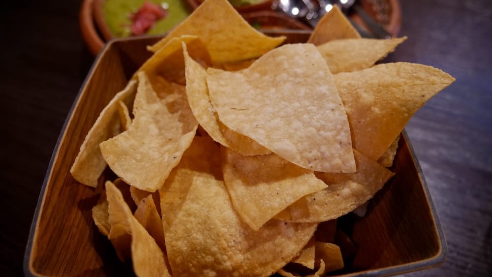 Tortilla chips at Añejo Banff with five-salsa starter during our Mexican lunch in Alberta, Canada Close-up of tortilla chips served at Añejo in Banff, Alberta, Canada, in a wooden bowl with part of the five-salsa-style starter visible behind them on the table.