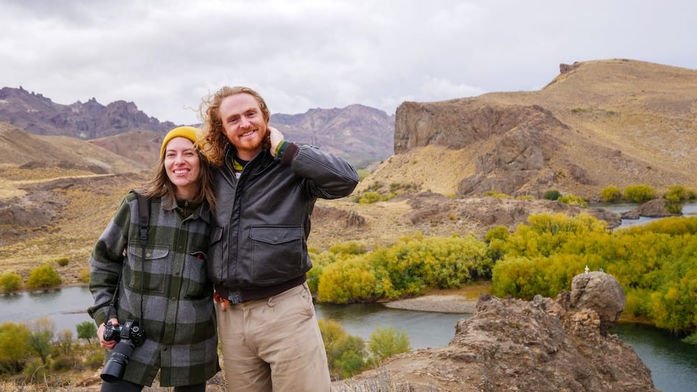 Samuel Jeffery and Audrey Bergner standing in Arroyo Verde Patagonia with wind visibly whipping their hair and clothing, surrounded by exposed steppe and river terrain that offers little protection from the region’s constant and powerful gusts.
