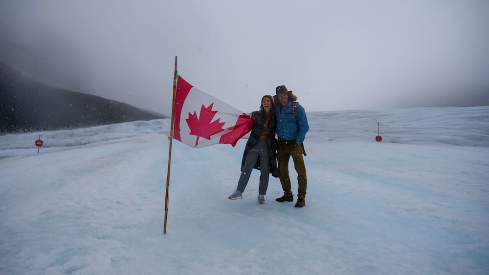 Samuel Jeffery y Audrey Bergner en el glaciar Athabasca, Columbia Icefield, en una tormenta de nieve — Alberta, Canadá Samuel Jeffery y Audrey Bergner sosteniendo una bandera canadiense en el glaciar Athabasca en el Columbia Icefield durante una tormenta de nieve, cayendo nieve y neblina limitando la visibilidad, Alberta, Canadá.