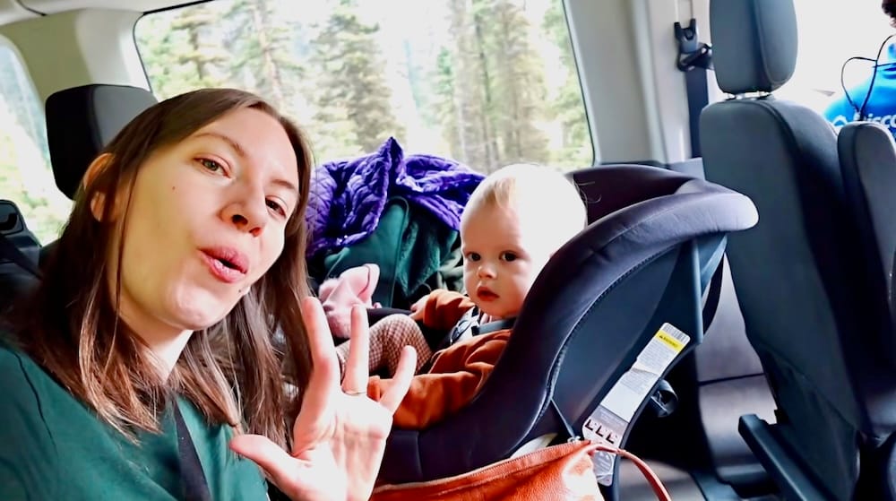 Audrey Bergner waves from inside a tour van on Moraine Lake Road in Banff National Park, Alberta, Canada, with baby Aurelia Jeffery seated in a car seat beside her.
