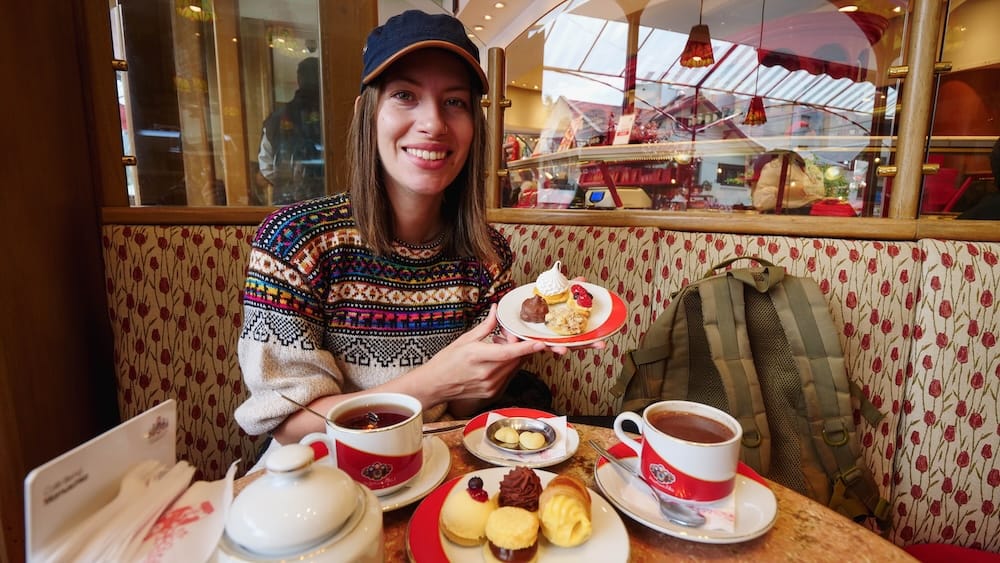 Audrey Bergner enjoying a sweet breakfast in San Carlos de Bariloche with tea, pastries, and dulce de leche desserts at a café, highlighting Patagonia’s indulgent morning food culture where sweets often replace traditional breakfast options
