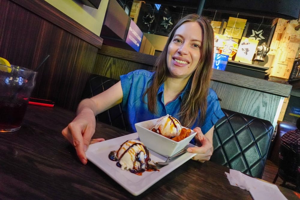 Audrey Bergner with dessert poutine at a sports bar, ICE District, Edmonton, Alberta, Canada Audrey Bergner presenting a plate of dessert poutine topped with ice cream, chocolate, and caramel glaze at a sports bar in the ICE District, Edmonton, Alberta, Canada.