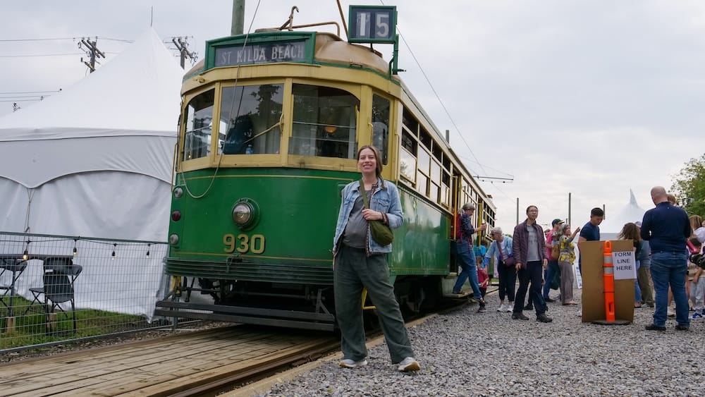 Audrey Bergner beside heritage streetcar 930 in Old Strathcona, Edmonton, Alberta, Canada Audrey Bergner standing beside green-and-cream heritage streetcar 930 near the Old Strathcona Fringe grounds, with festival tents and visitors behind her in Edmonton, Alberta, Canada.