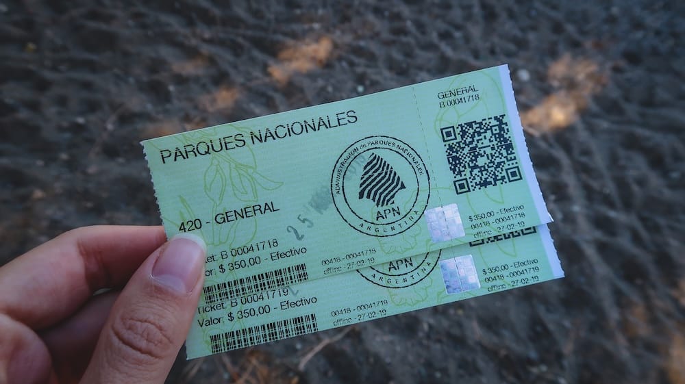 Audrey Bergner Holding National Park Tickets Near San Martín de los Andes, Patagonia Audrey Bergner holds two Argentine national park entrance tickets near a dark volcanic-sand beach outside San Martín de los Andes, Neuquén, Patagonia, Argentina.