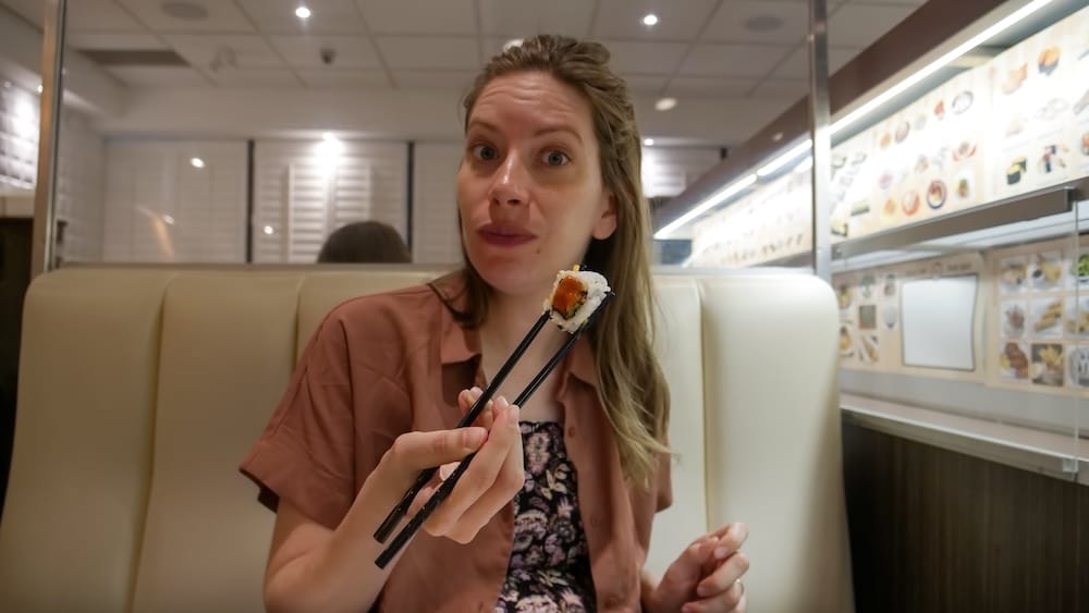 Audrey Bergner sosteniendo una pieza de sushi con palitos en un box de Point Sushi en Calgary, Alberta, Canadá, con el menú de la tablet a la vista en el fondo.