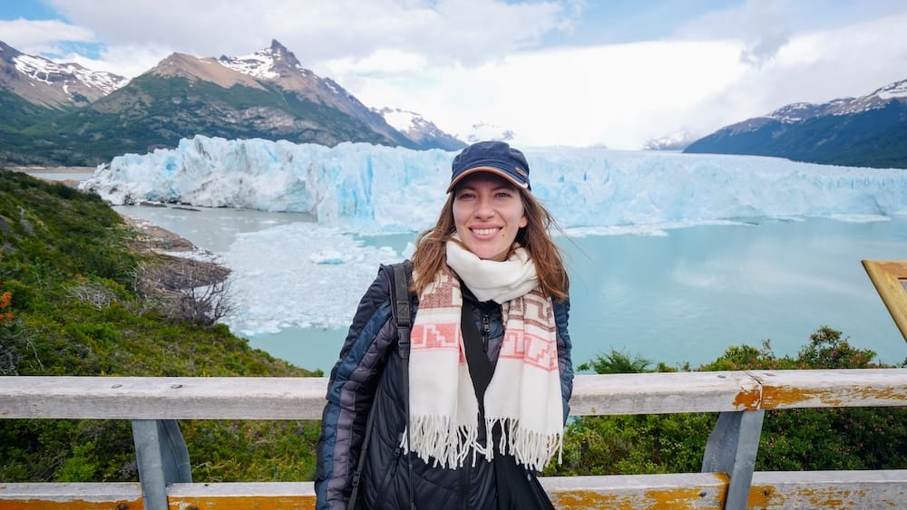 Audrey Bergner sonríe en un mirador del glaciar Perito Moreno, con el enorme muro de hielo azul y blanco, el Lago Argentino y montañas escarpadas detrás, en Santa Cruz, Argentina.