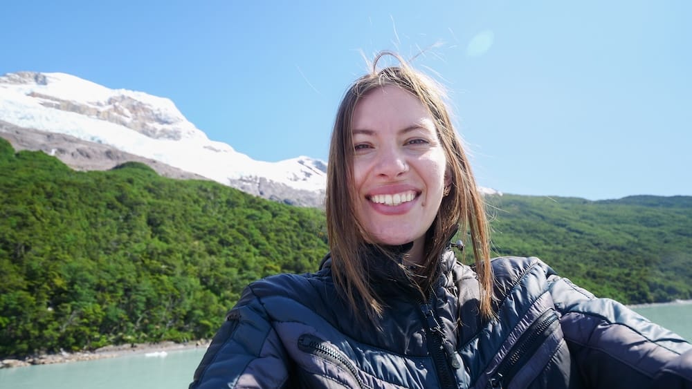 Audrey Bergner at Perito Moreno Glacier near El Calafate in Santa Cruz, Patagonia, Argentina Audrey Bergner smiles beside the turquoise waters and forested slopes near Perito Moreno Glacier, with snow-covered ice and a bright blue sky in Santa Cruz, Patagonia, Argentina.
